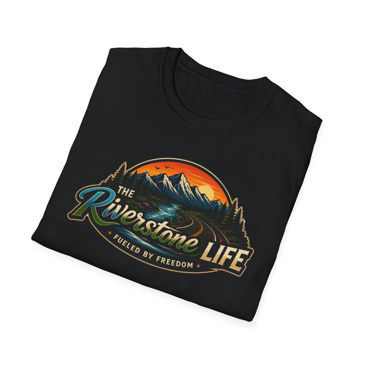 A black folded t-shirt with a retro-style scenic graphic on the front. The graphic features mountains, a winding river, pine trees, and an orange sunset, with the text 'The Riverstone Life' and 'Fueled by Freedom'.