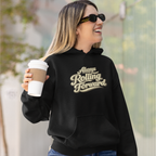 A woman wearing a black hoodie with the phrase 'Always Rolling Forward' printed in a beige retro-style font on the chest. She is holding a white coffee cup and wearing sunglasses, set against a blurred outdoor background.