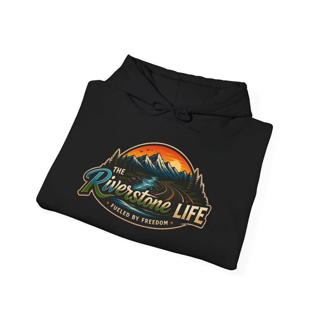 A black folded hoodie on a white background, featuring a large graphic print on the front with mountains, a river, and the text 'The Riverstone Life- Fueled by Freedom' and 'Fueled by Freedom'.