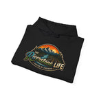 A black folded hoodie on a white background, featuring a large graphic print on the front with mountains, a river, and the text 'The Riverstone Life- Fueled by Freedom' and 'Fueled by Freedom'.
