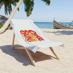 A white beach towel draped over a wooden lounge chair on a sandy beach, featuring a retro-style red and orange graphic that reads 'Chase the Sun'.