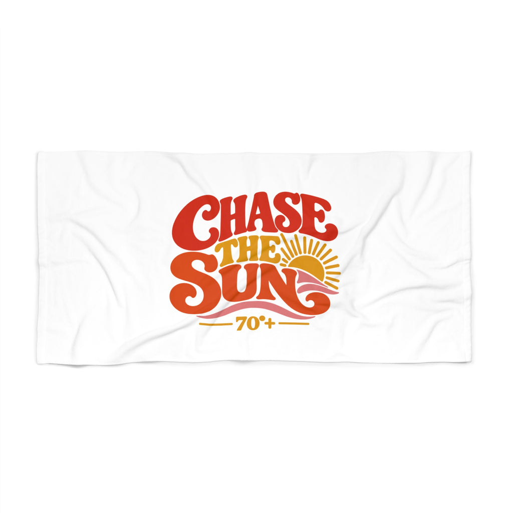 A white rectangular towel or beach blanket with a retro-style graphic reading 'CHASE THE SUN' in red, orange, and yellow, plus '70+' and a sun illustration, shown on a plain white background.