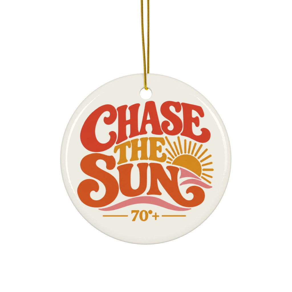 A round ceramic Christmas ornament with a white glossy background, featuring retro-style text that reads 'CHASE THE SUN' in red and orange, with a yellow sun graphic and '70+' below. The ornament hangs from a gold string against a plain white background.