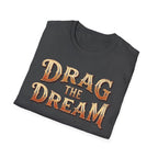 A folded dark heather t-shirt with a distressed orange and gold graphic text reading 'DRAG THE DREAM' on a clean white background.