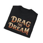 A black folded t-shirt with a distressed graphic reading 'DRAG THE DREAM' in orange and beige lettering, displayed on a clean white background.