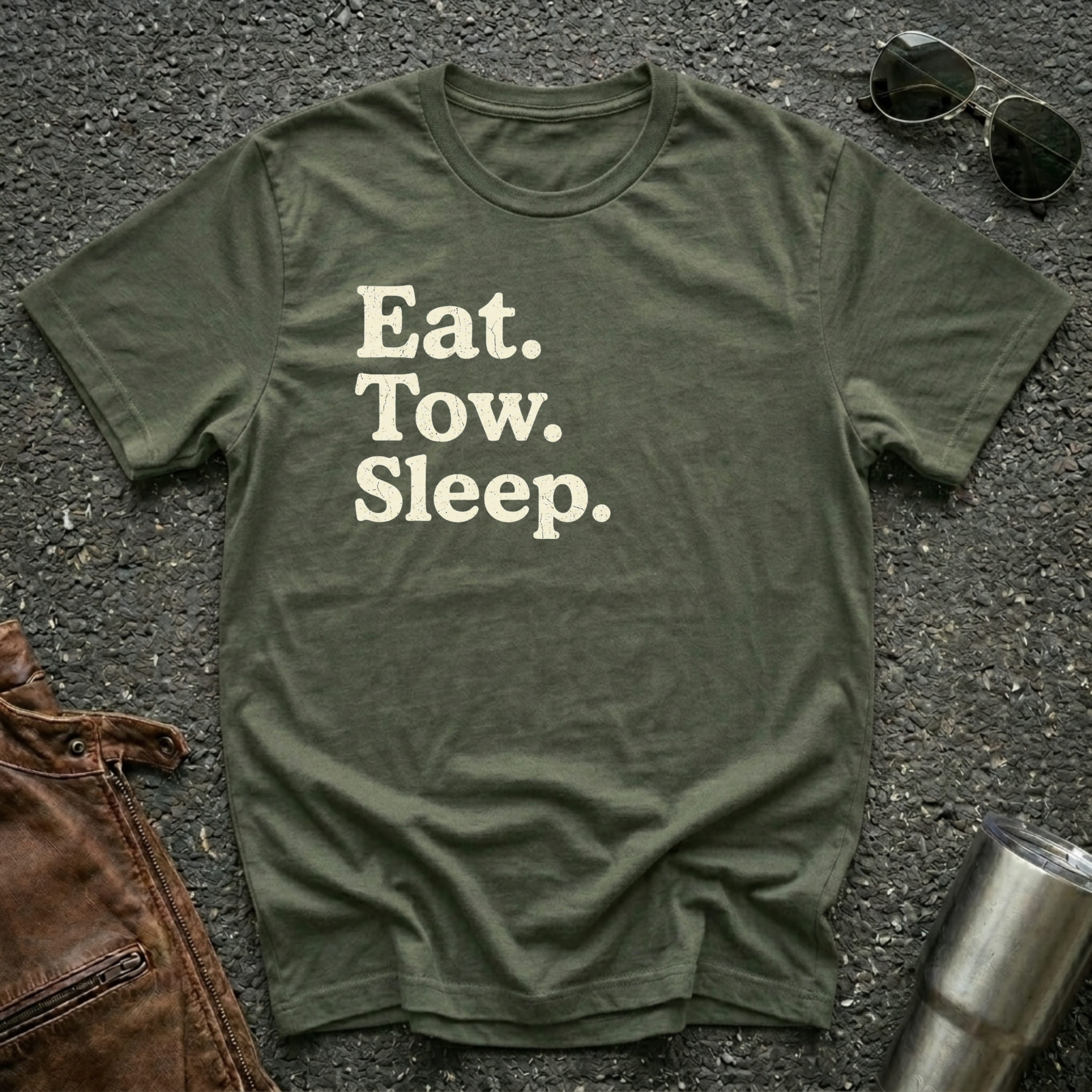 A military green crewneck t-shirt with the text 'Eat. Tow. Sleep.' flat lay.