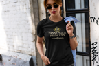 A woman wearing a black graphic t-shirt with a gold crown and 'PASSENGER PRINCESS' text, standing in an urban alleyway.