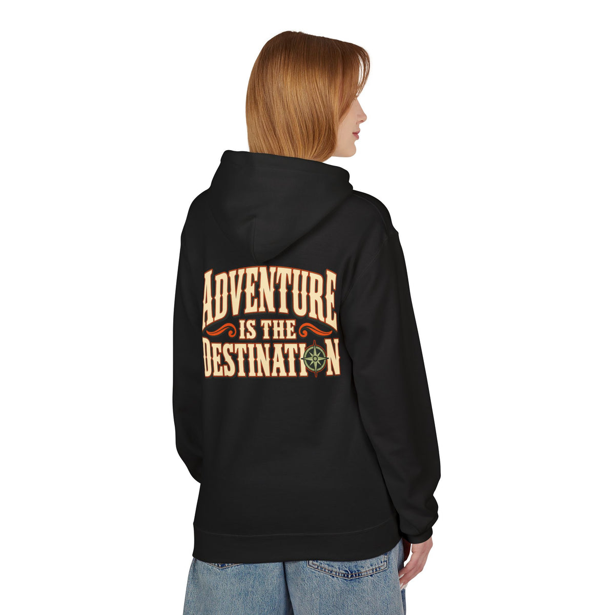 A woman shown from the back wearing a black hoodie with a large vintage-style graphic on the back that reads 'ADVENTURE IS THE DESTINATION' in tan and orange lettering with a small compass design. She is also wearing light blue jeans against a plain white background.