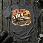 Haul Yeah RV Transport T-shirt by The Riverstone Life on a dark heather Gildan Softstyle 64000 featuring a pickup truck towing a fifth-wheel RV.