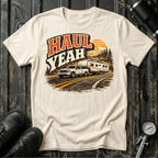 Haul Yeah RV Transport T-shirt by The Riverstone Life on a natural Gildan Softstyle 64000 featuring a pickup truck towing a fifth-wheel RV.