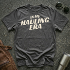 Dark heather 'In My Hauling Era' road life t-shirt featuring bold cream typography on a soft unisex tee.
