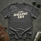 Dark heather 'In My Hauling Era' road life t-shirt featuring bold cream typography on a soft unisex tee.