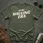 Military green 'In My Hauling Era' road life t-shirt featuring bold cream typography on a soft unisex tee.
