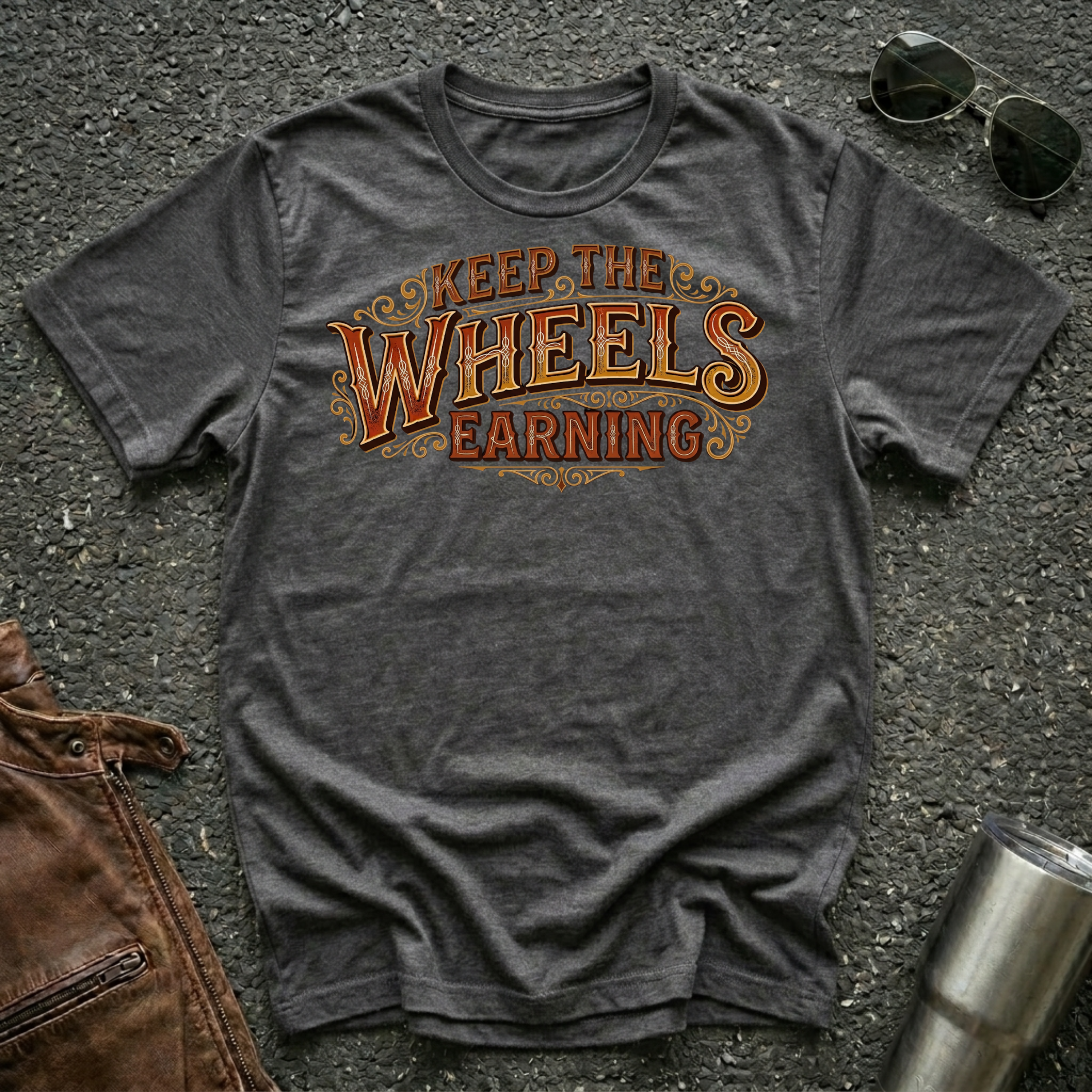 Dark heather 'Keep The Wheels Earning' RV Transport T-shirt featuring vintage gold and rust typography on a soft unisex tee.