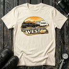 Loaded Up & Pointed West T-shirt by The Riverstone Life on a natural Gildan Softstyle 64000 featuring a pickup truck towing a camper toward a western sunset.