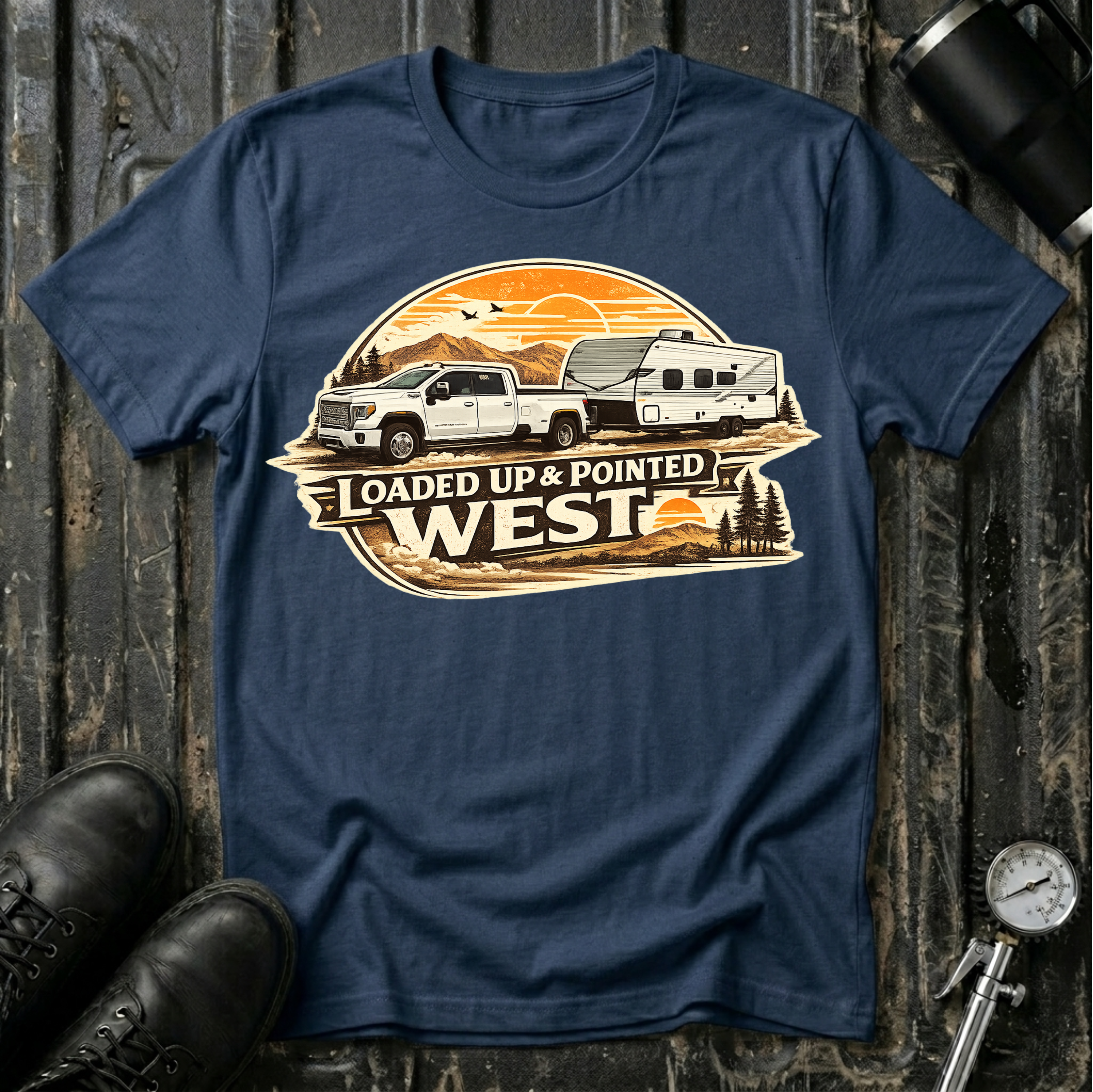 Loaded Up & Pointed West T-shirt by The Riverstone Life on a navy Gildan Softstyle 64000 featuring a pickup truck towing a camper toward a western sunset.