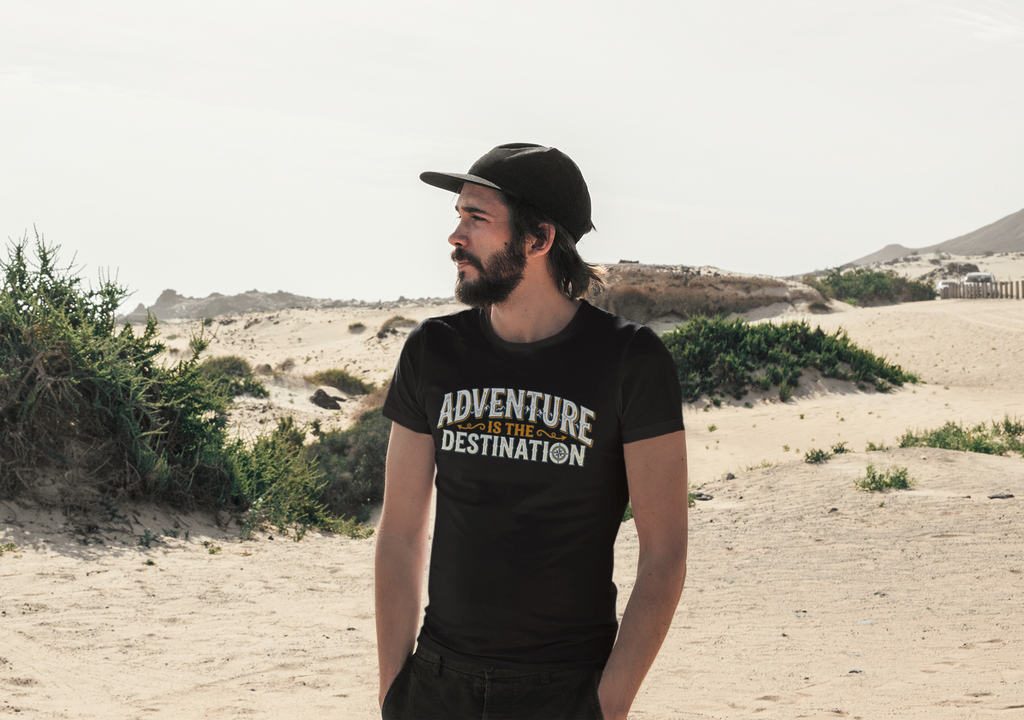 A man wearing a black t-shirt with 'ADVENTURE IS THE DESTINATION' printed on the front, standing in a sandy desert landscape.