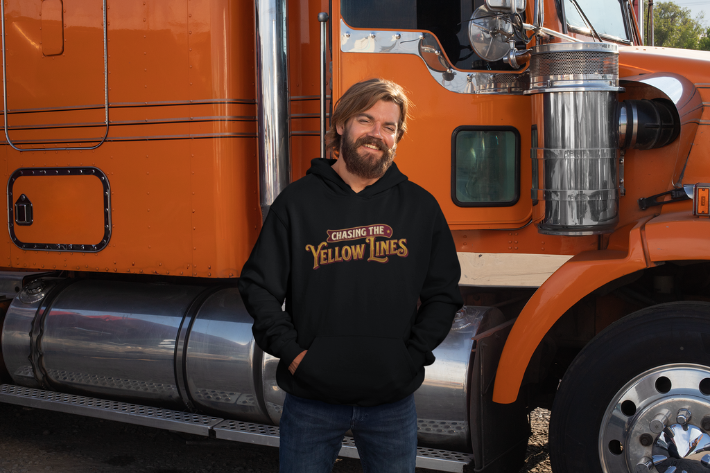 A man with a beard wearing a black hoodie with 'Chasing the Yellow Lines' printed on the chest, standing in front of an orange semi-truck.