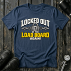 A navy blue graphic t-shirt laid flat on a dark wood background, styled with black leather boots, a black tumbler, and a pressure gauge. The shirt features a graphic print of a padlock and chains with the text 'LOCKED OUT OF THE LOAD BOARD AGAIN!' in white and yellow.