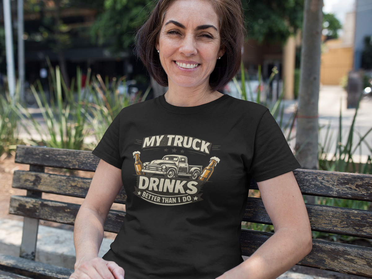 A woman sitting on a wooden bench outdoors wearing a black graphic t-shirt with a vintage truck and beer bottles design that reads 'MY TRUCK DRINKS BETTER THAN I DO'.