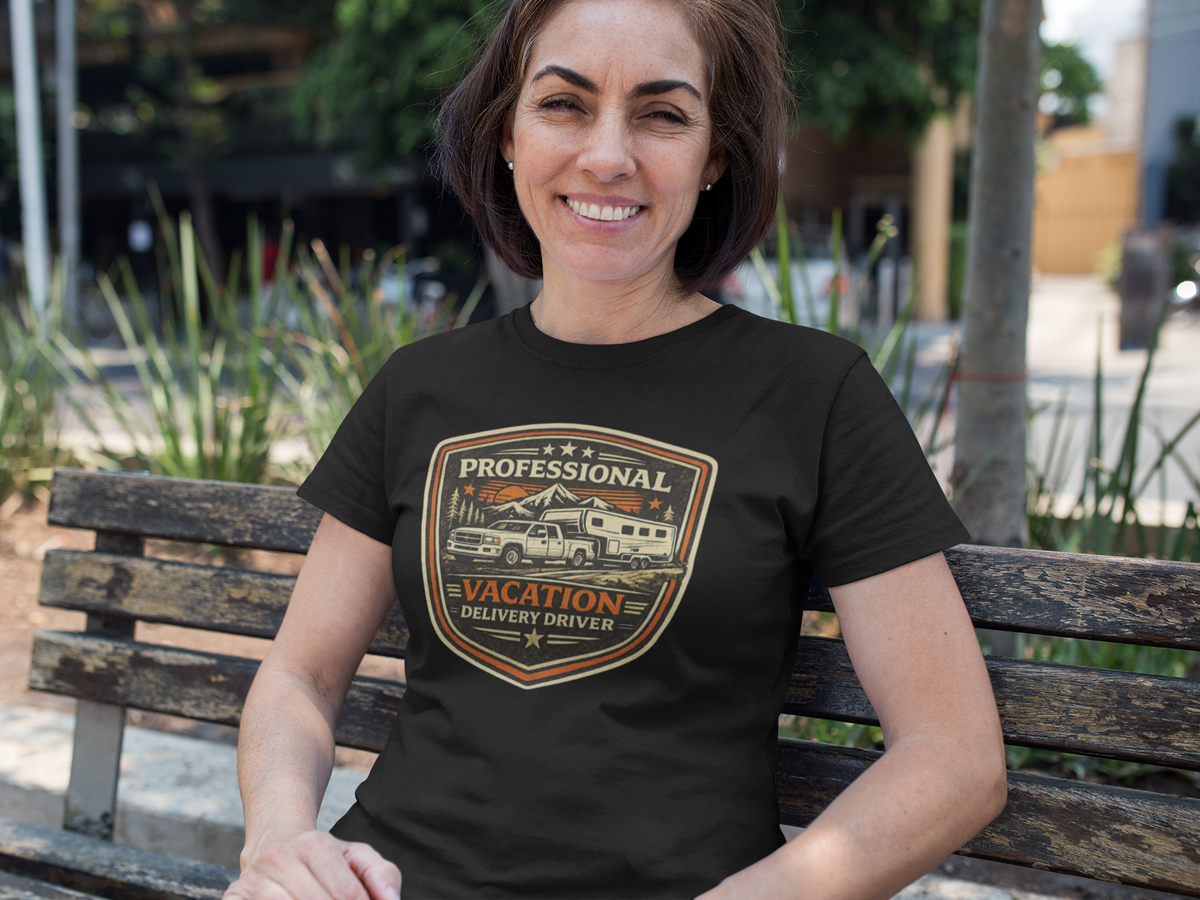 A woman sitting on a wooden bench outdoors wearing a black t-shirt with a vintage-style American flag and camper graphic that reads 'Professional Vacation Delivery Driver'.