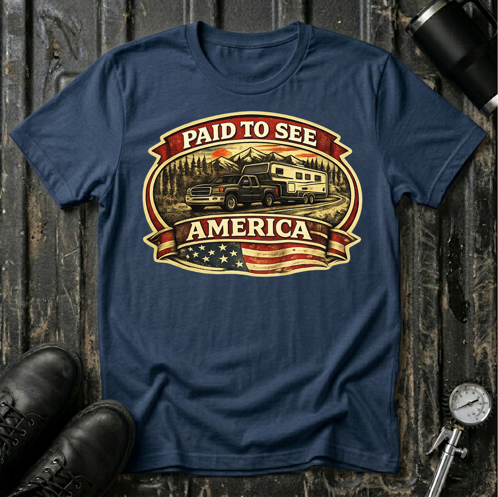 Paid to See America dark truck T-shirt by The Riverstone Life on a navy Gildan Softstyle 64000 featuring a pickup truck hauling a fifth-wheel with an American flag and scenic landscape.
