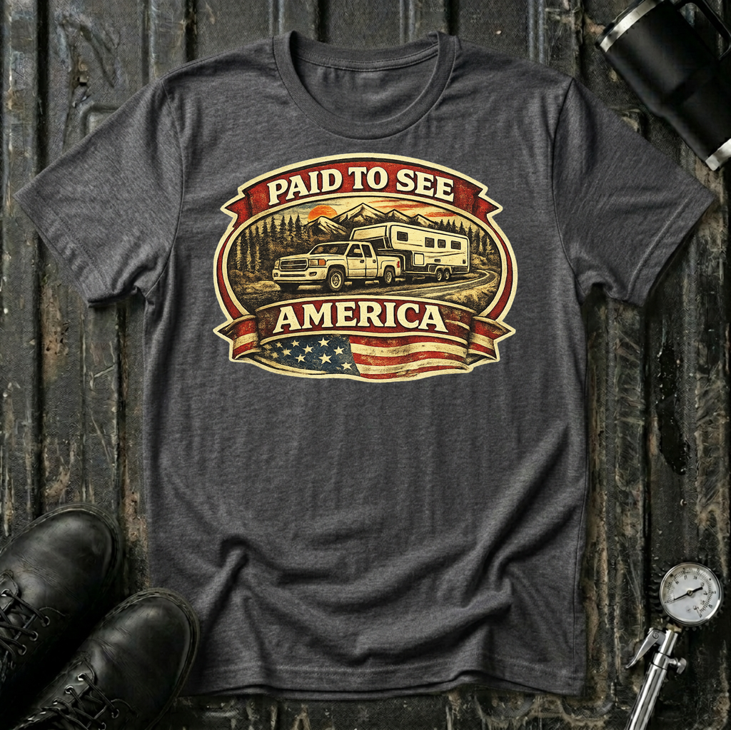Paid to See America light truck T-shirt by The Riverstone Life on a dark heather Gildan Softstyle 64000 featuring a pickup truck hauling a fifth-wheel with an American flag and scenic landscape.