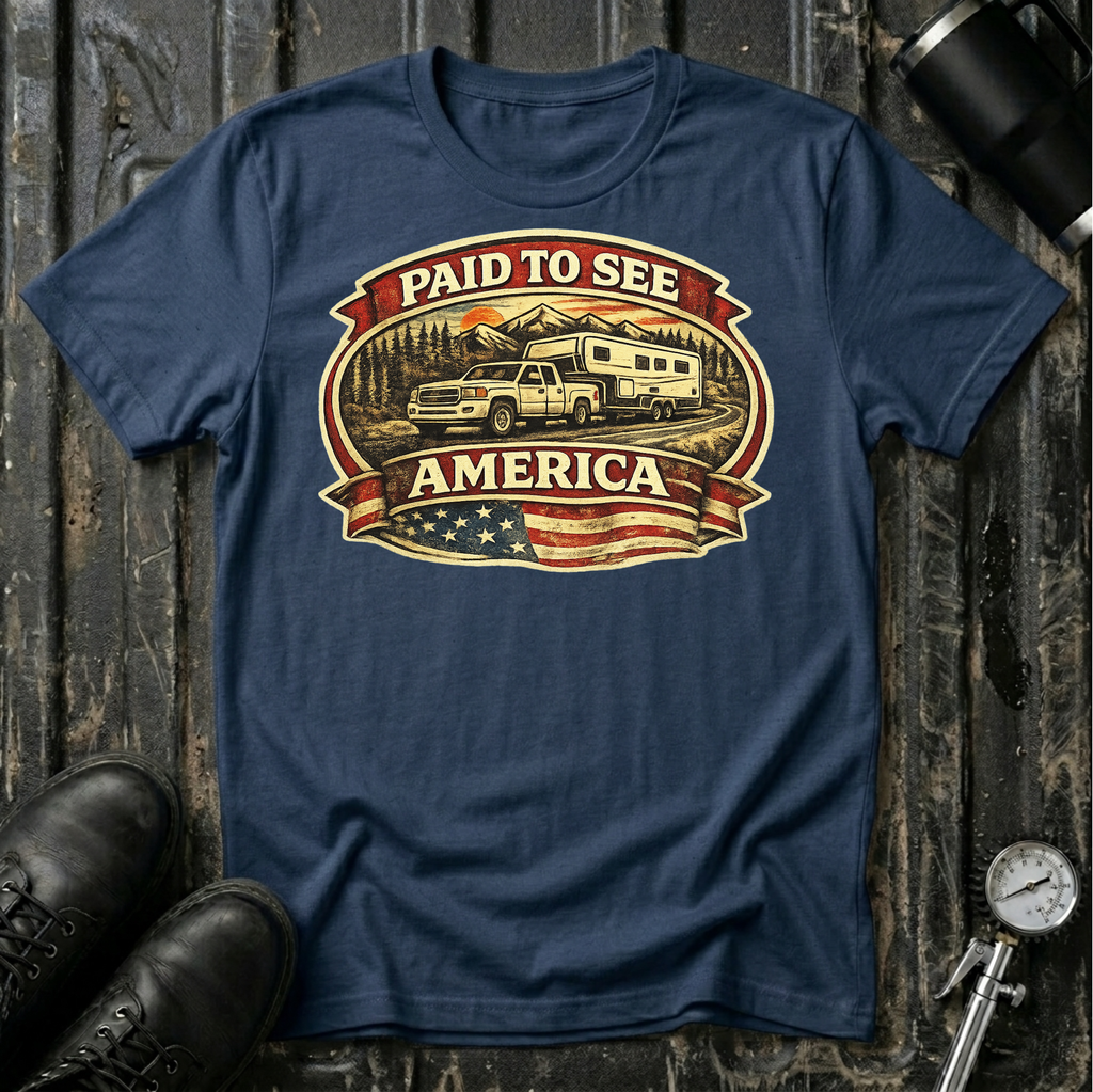Paid to See America light truck T-shirt by The Riverstone Life on a navy Gildan Softstyle 64000 featuring a pickup truck hauling a fifth-wheel with an American flag and scenic landscape.