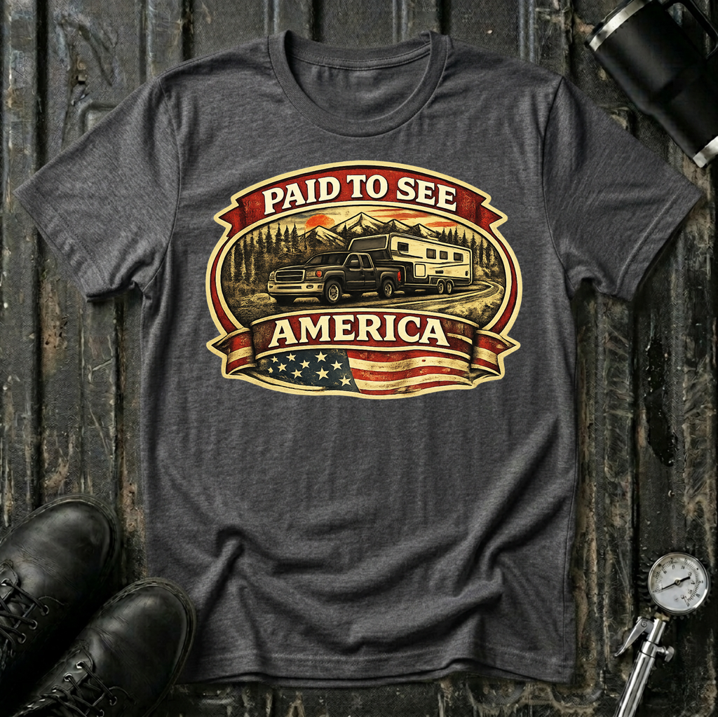 Paid to See America dark truck T-shirt by The Riverstone Life on a dark heather Gildan Softstyle 64000 featuring a pickup truck hauling a fifth-wheel with an American flag and scenic landscape.