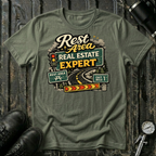 Rest Area Real Estate Expert T-shirt by The Riverstone Life featuring a military green Gildan Softstyle 64000 featuring a humorous highway and rest area design for RV Transport drivers and road travelers.
