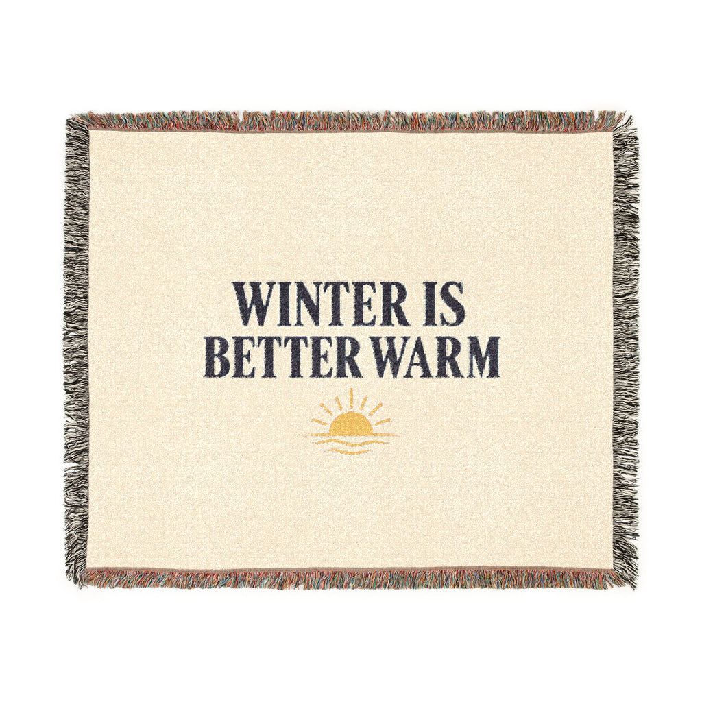 A square woven throw blanket with a cream-colored center, featuring the text 'WINTER IS BETTER WARM' in dark navy blue, a small yellow sun graphic, and multicolor fringed edges.
