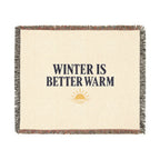 A square woven throw blanket with a cream-colored center, featuring the text 'WINTER IS BETTER WARM' in dark navy blue, a small yellow sun graphic, and multicolor fringed edges.